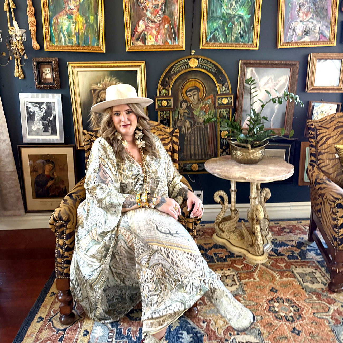 Artist Mari Toscas aka The Pine Torch sitting in a room full of art.