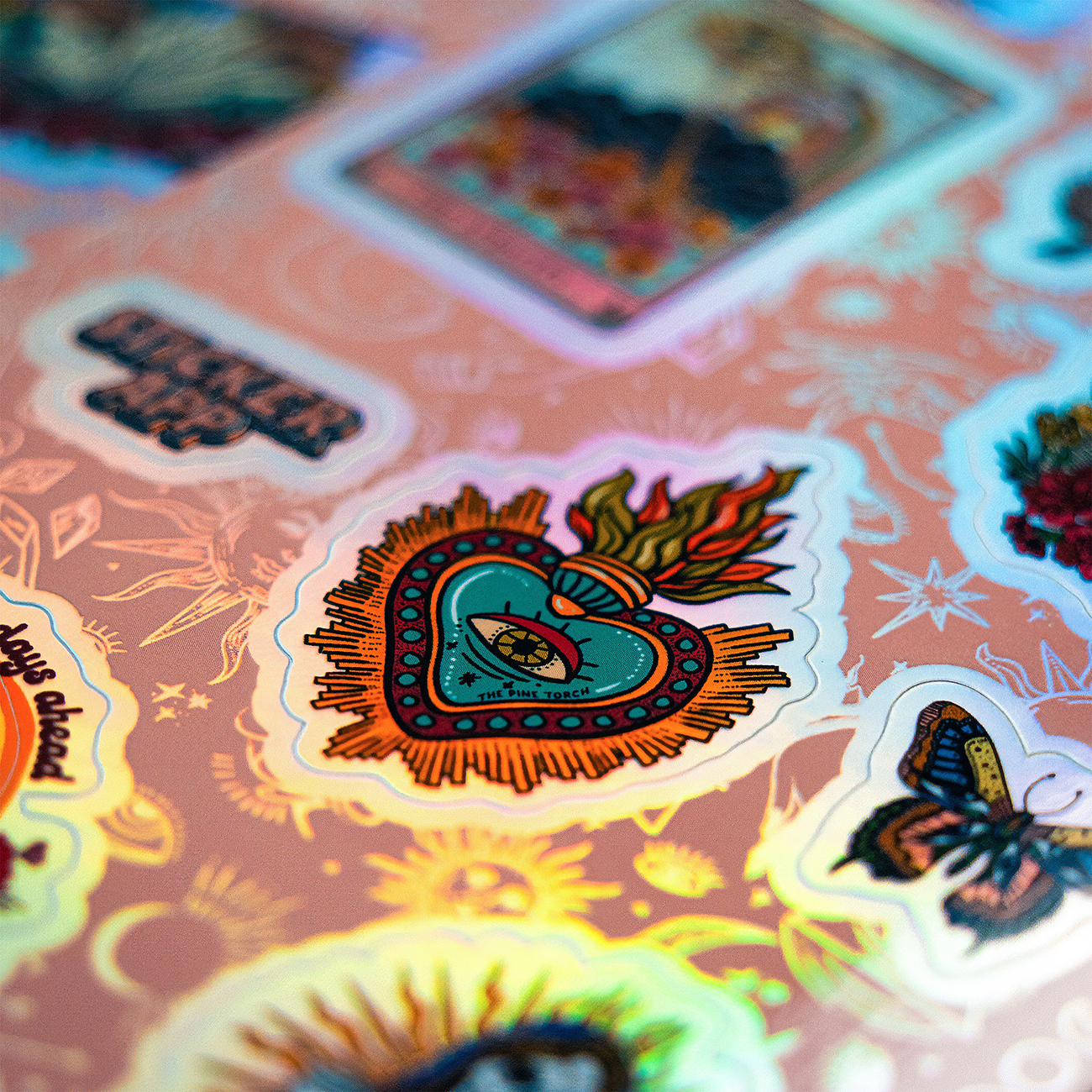 Holographic sticker sheet with a burning heart design surrounded by a butterfly, a card design and StickerApp logo.