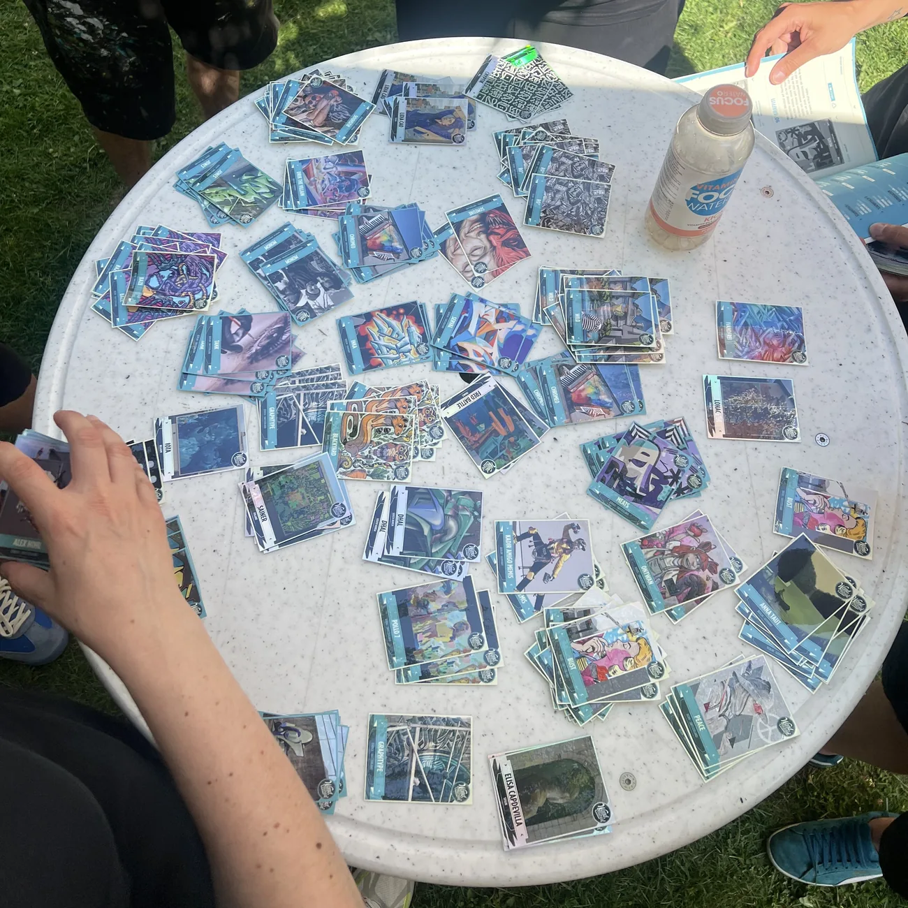 Visitantes do festival preenchem cadernetas azuis com autocolantes colecionáveis de arte urbana espalhados numa mesa redonda
