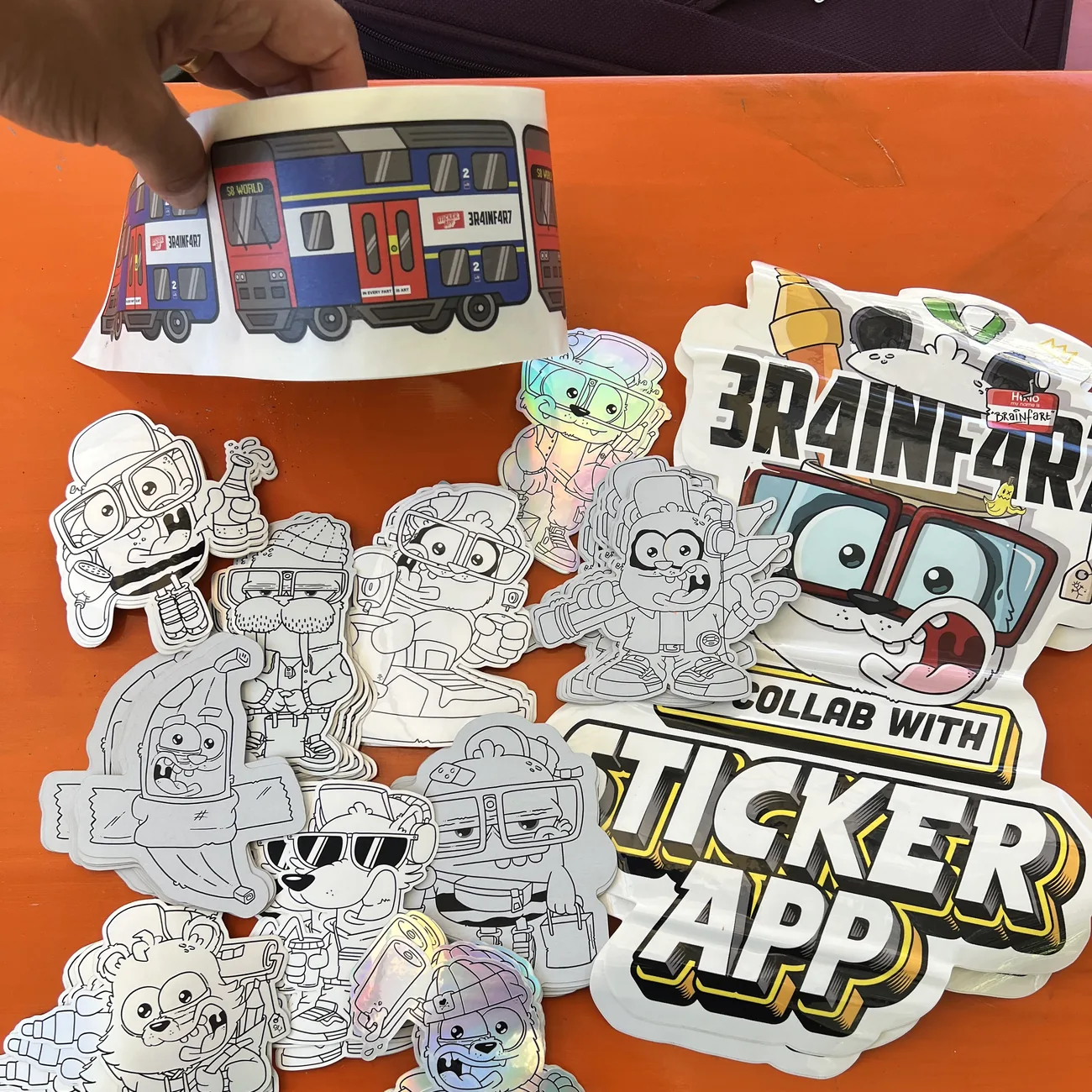 Etiqueta do comboio S8 World Brainfart x StickerApp com a placa "In every fart is art", segurada por cima de autocolantes recortados a preto e branco