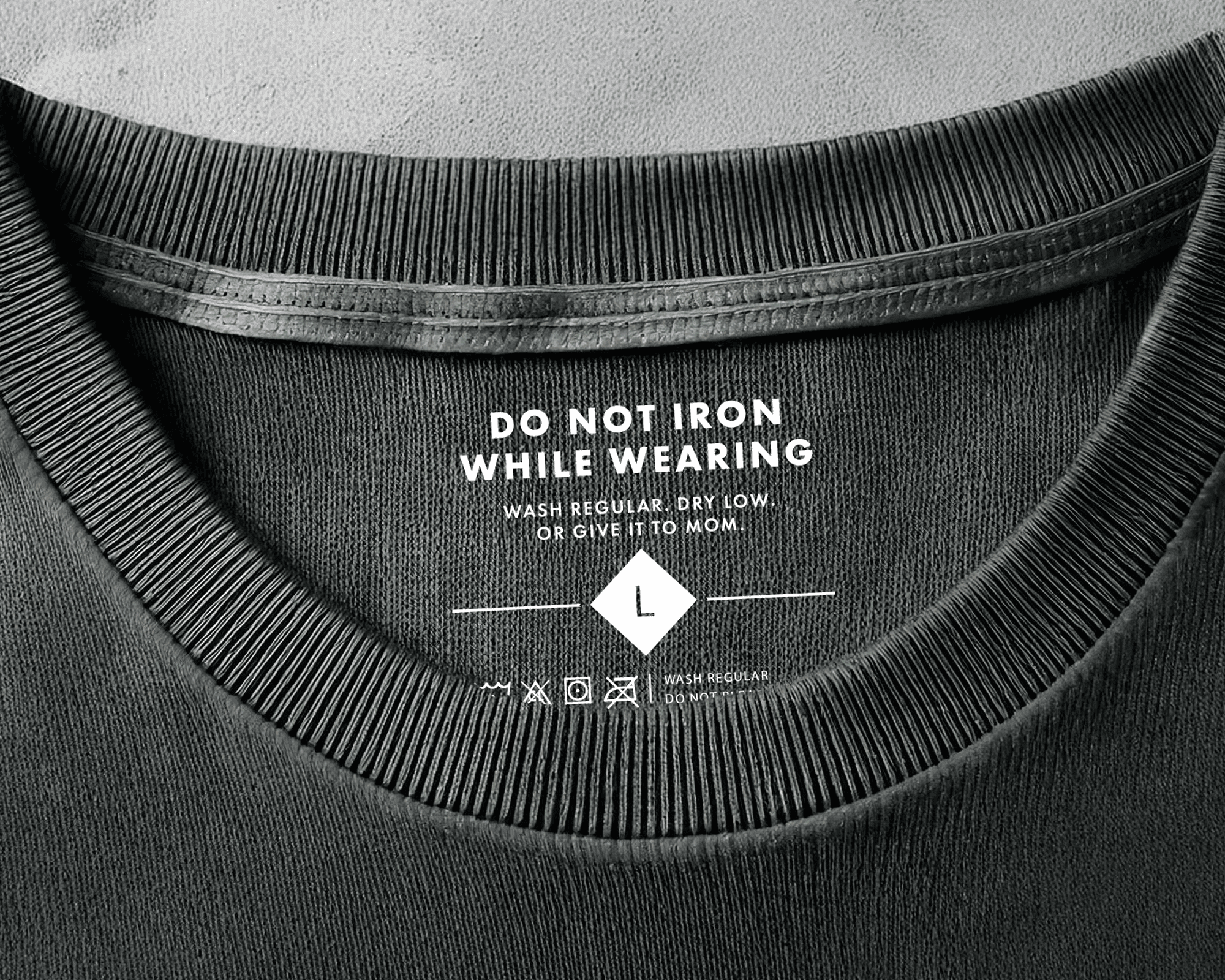 Close-up of a black shirt's collar with a humorous heat transfer: "Do not iron while wearing. Wash regular, dry low, or give it to mom."